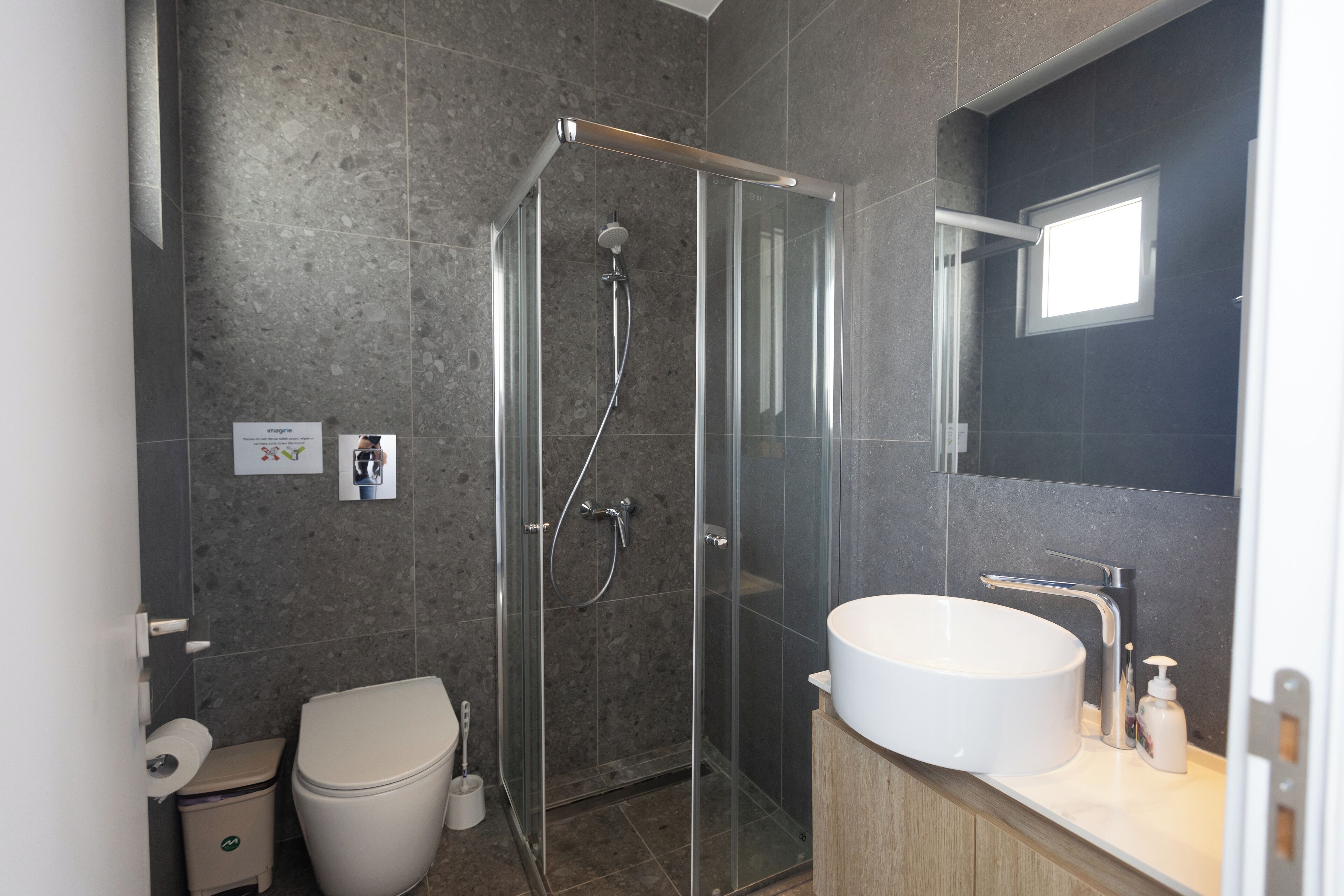 Une salle de bain moderne avec une douche à parois de verre, un lavabo blanc et un mur recouvert de carreaux foncés.