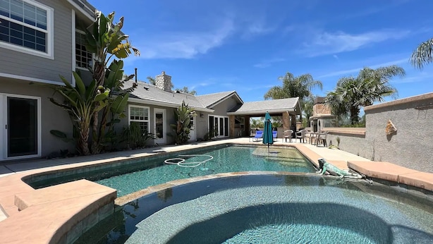 A swimming pool with a stone border, surrounded by a patio area with outdoor furniture and a covered seating area. - Villa 5B/3B with pool/spa/mini golf putting (Temecula)