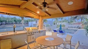 An outdoor kitchen area with a grill, sink, and dining table with chairs. - Villa 5B/3B with pool/spa/mini golf putting (Temecula)