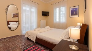 Een hotelkamer met een bed, een nachtkastje met lamp, een televisie, een spiegel en een raam met gordijnen.