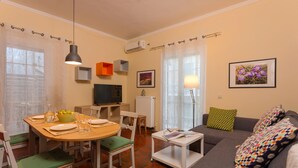 Een woonkamer met een eettafel, stoelen, een bank en een televisie.