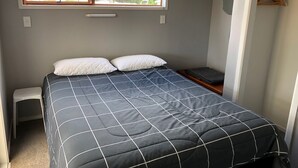 A bedroom with a bed, a window, a closet, and a small stool.