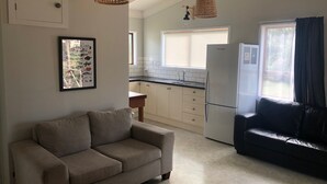 A modern kitchen with white cabinets, a black countertop, and a refrigerator. There is a beige sofa and a black leather sofa in the living area.