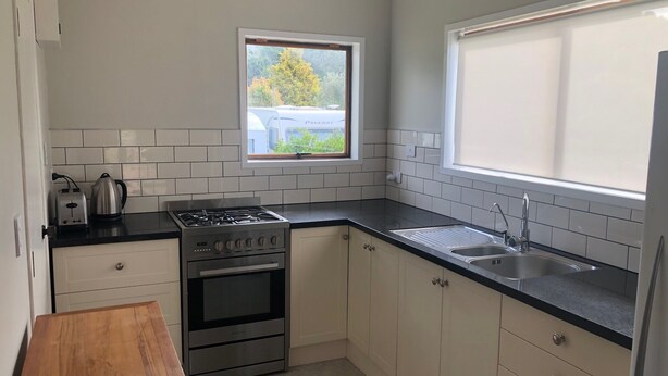 A compact kitchen with white cabinets, a black countertop, a gas stove, a built-in oven, a sink, and a window with a view of trees.
