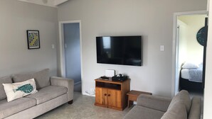 A living room with a grey sofa, a wooden cabinet, and a flat-screen TV mounted on the wall.
