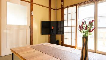 A room with a tatami mat floor, a television, a vase with flowers, and a sliding door with a view outside.