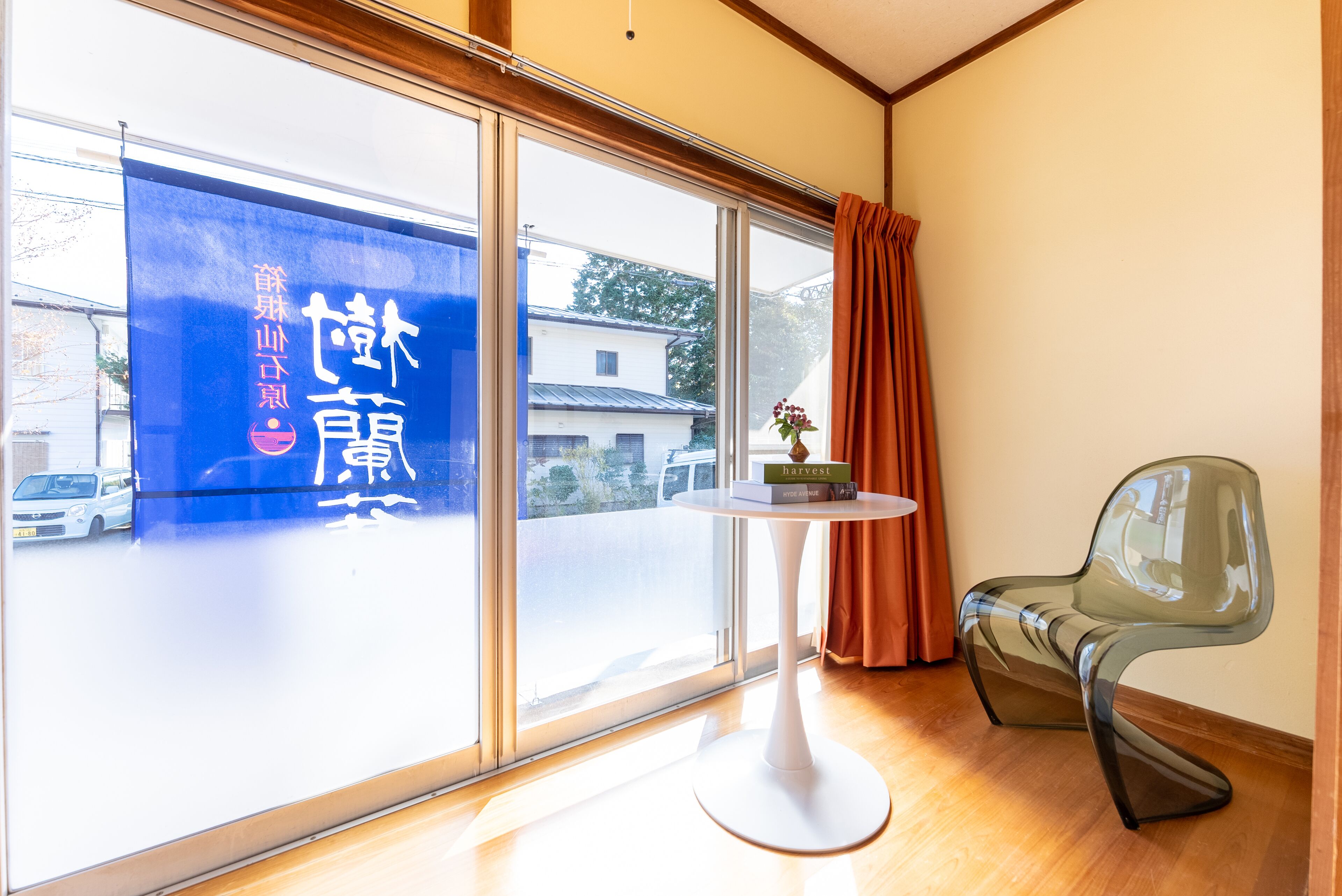 A room with a large sliding glass door, a small round table with a book, a modern chair, and a curtain.