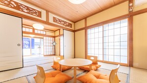 Una habitación japonesa tradicional con suelo de tatami, una mesa redonda y cojines anaranjados.