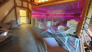 Een spa-ruimte met massagetafels, een houten plafond en een paars verlichte wand.