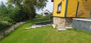 Une maison jaune avec un escalier en pierre menant à une porte, entourée d’une pelouse bien entretenue et d’une clôture.