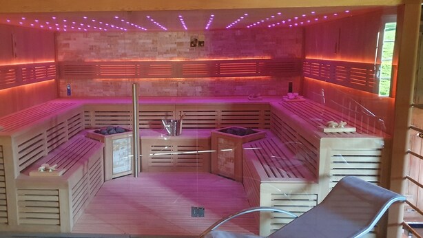 Een sauna met houten banken en een centrale pilaar, omgeven door wanden met ingebouwde verlichting.
