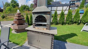 Een buitenoven van baksteen met schoorsteen, omgeven door een geplaveid terras.