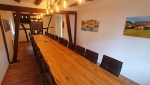 Een lange houten eettafel met zwarte stoelen, een open haard en lijstwerken aan de wanden.
