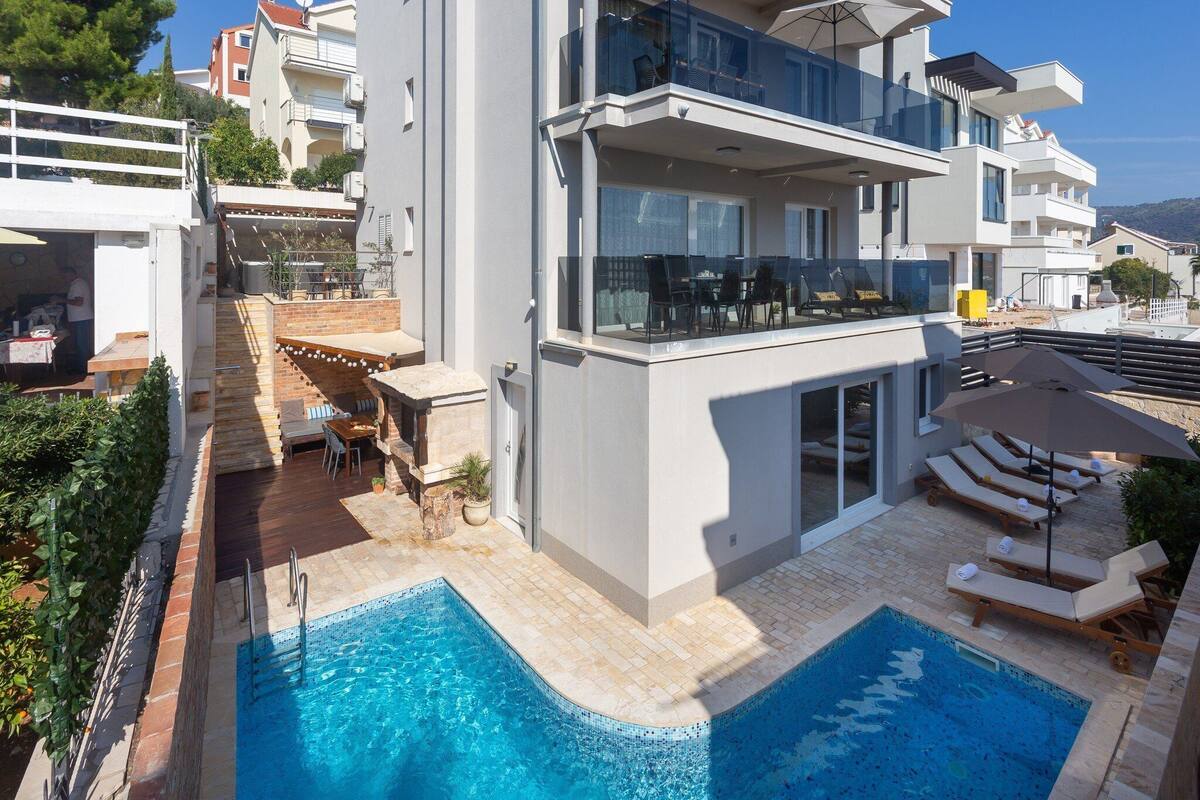 A modern two-story building with a rooftop pool area, outdoor seating, and a clear view of the surrounding landscape.