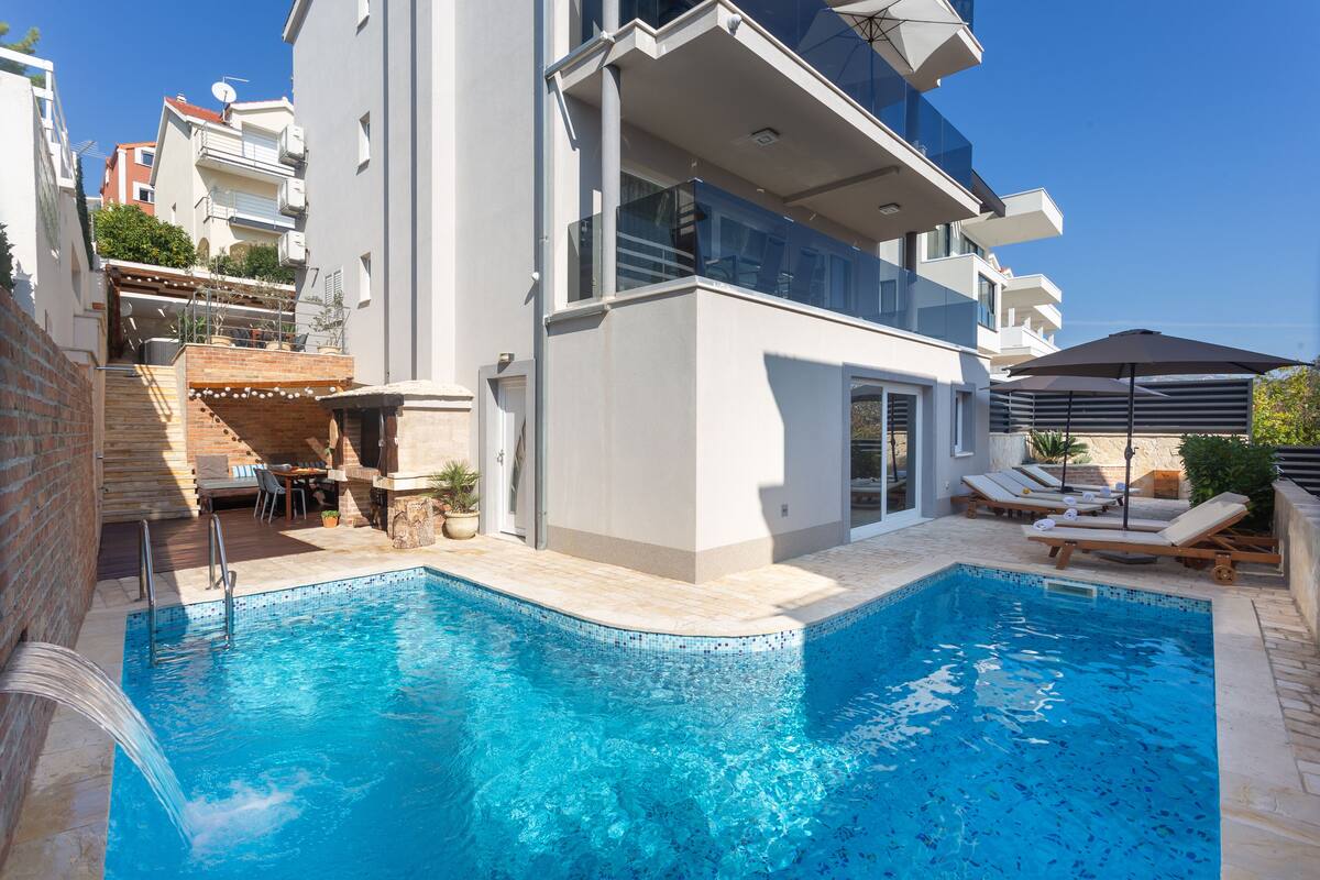 A modern building with a swimming pool, outdoor seating, and a clear blue sky.