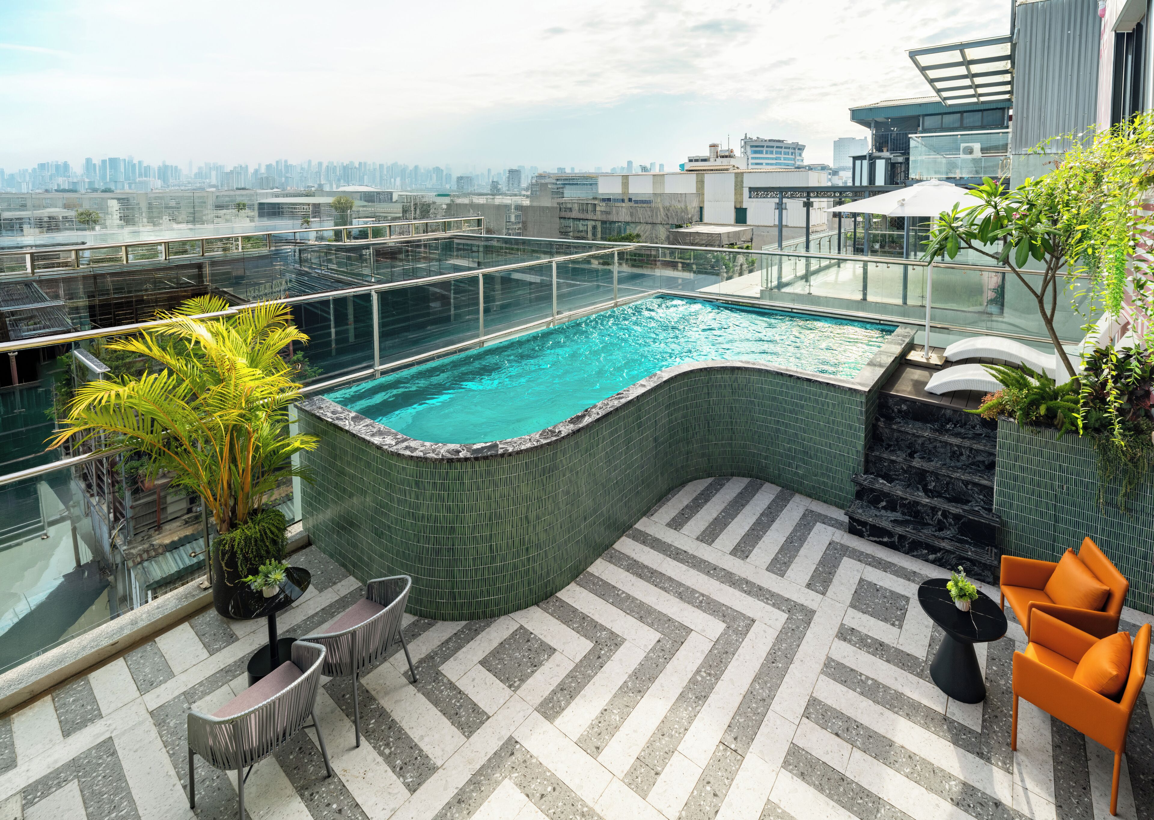 A rooftop pool with a city view, surrounded by outdoor seating and plants.