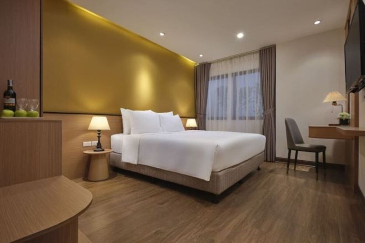 A hotel room with a bed, bedside tables, a desk, a chair, a TV, and a window with curtains.