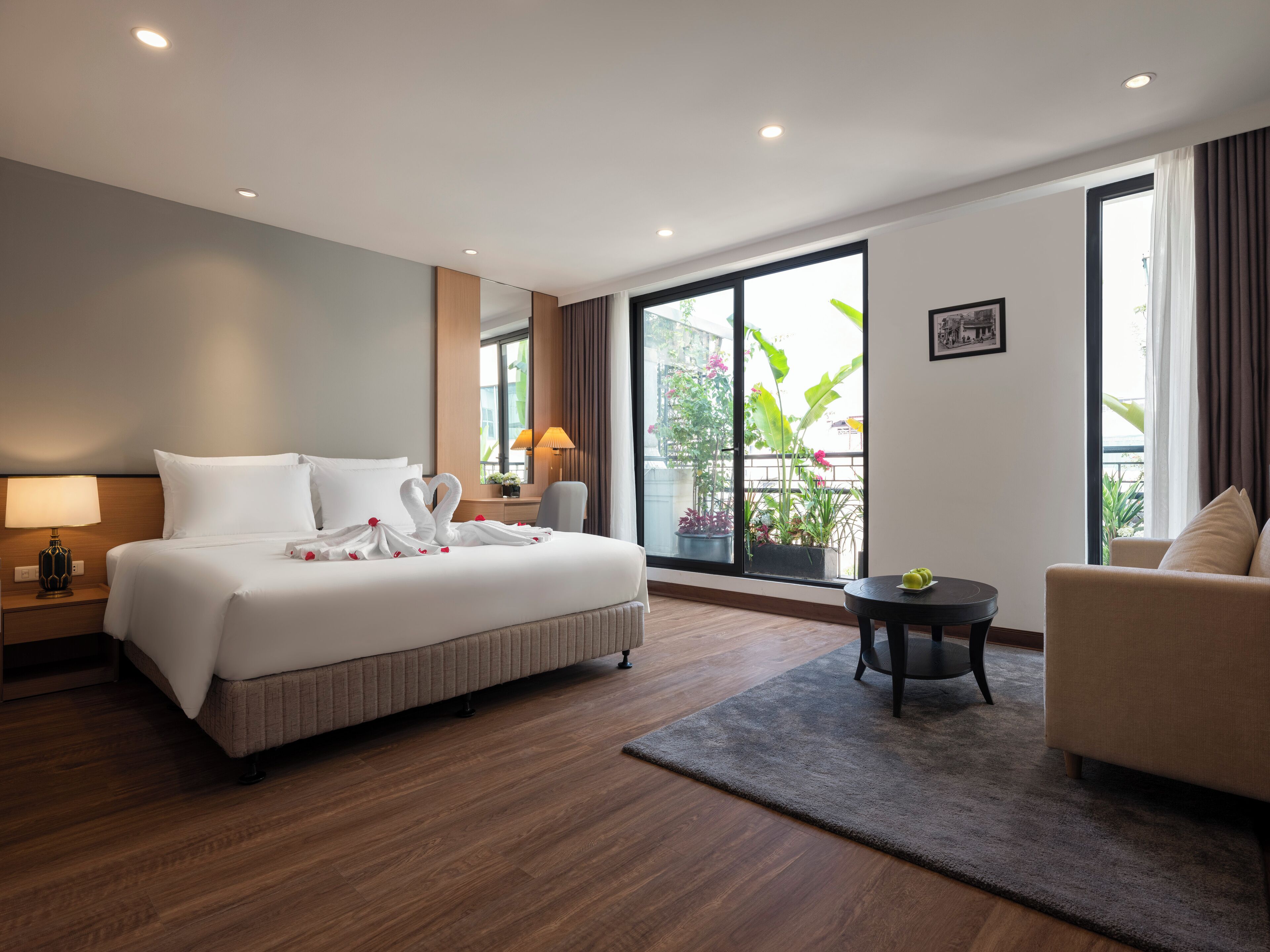 Een hotelkamer met een groot bed, een bureau, een stoel, een klein tafeltje en een balkon met planten.