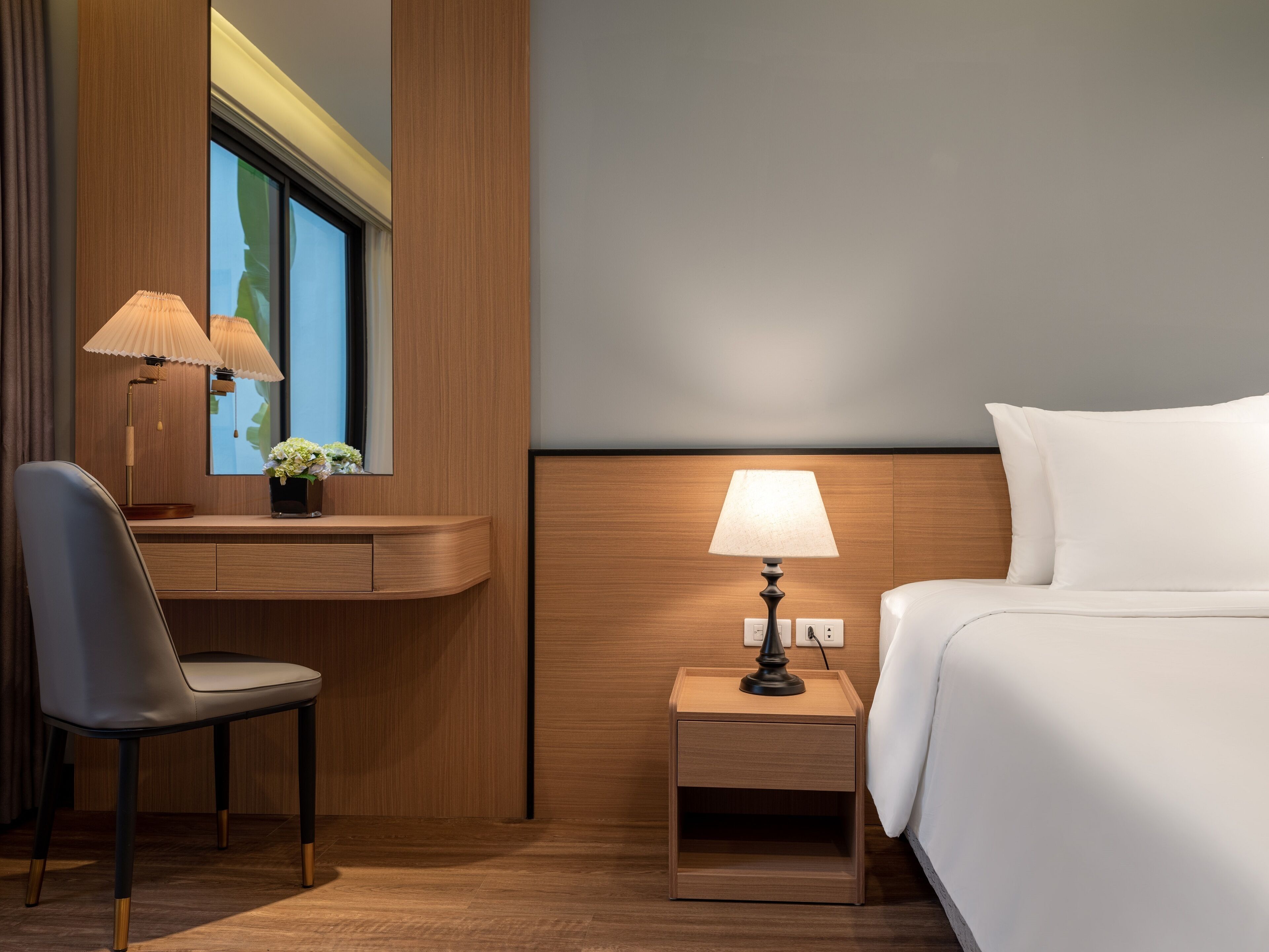 Une chambre d’hôtel comprenant un lit, un bureau avec une chaise, une table de chevet avec une lampe et une fenêtre donnant sur un paysage verdoyant.