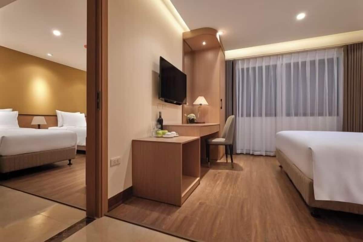 A hotel room with two beds, a desk, a chair, a TV, and a window with curtains.