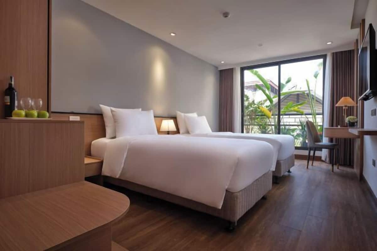 A modern hotel room with a large bed, bedside tables, a desk, and a view of greenery through the window.