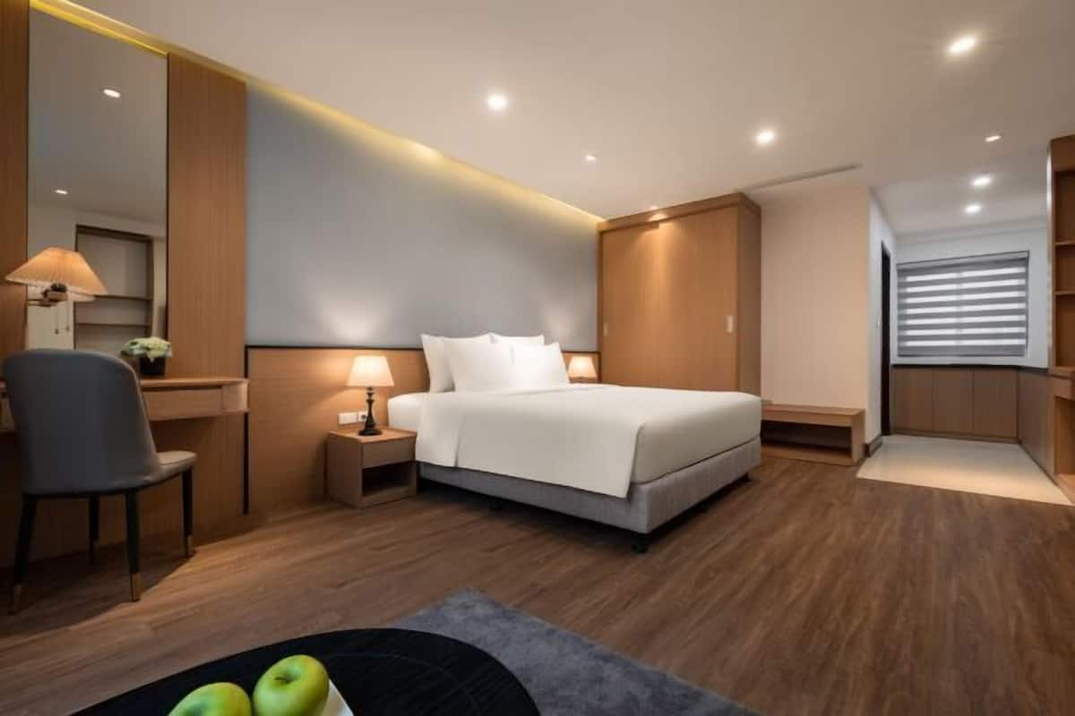 A modern hotel room with a bed, bedside table, lamp, chair, and a desk area.