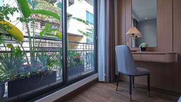 A modern hotel room with a large window, a chair, a bedside table with a lamp, and a mirror.