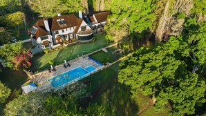 Una casa grande con piscina, rodeada de abundante vegetación y árboles.