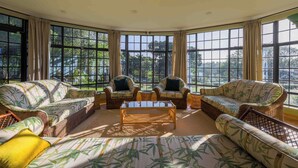 Una habitación con ventanas amplias, muebles de mimbre y una mesa de centro.
