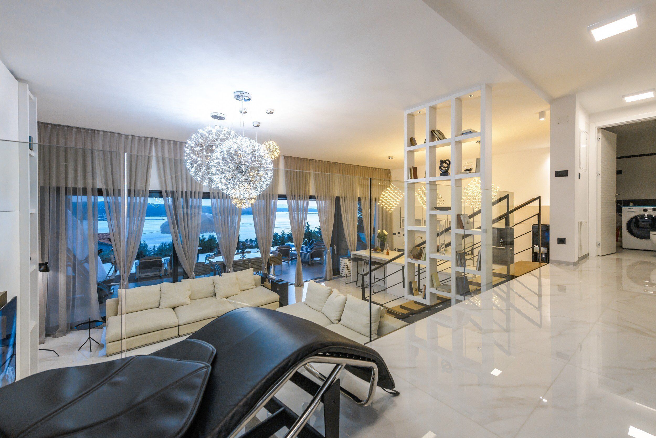 Sala de estar moderna com sofá, uma poltrona preta, escada e vista para o exterior.