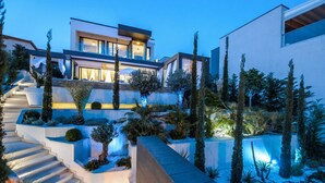 A modern house with a staircase leading to a balcony, surrounded by landscaped gardens and tall trees. - Villa Panorama (Crikvenica)