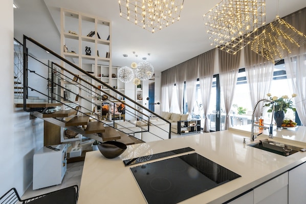 A modern kitchen with a central island, built-in appliances, and a staircase leading to a living area with a sofa and a dining table. - Villa Panorama (Crikvenica)