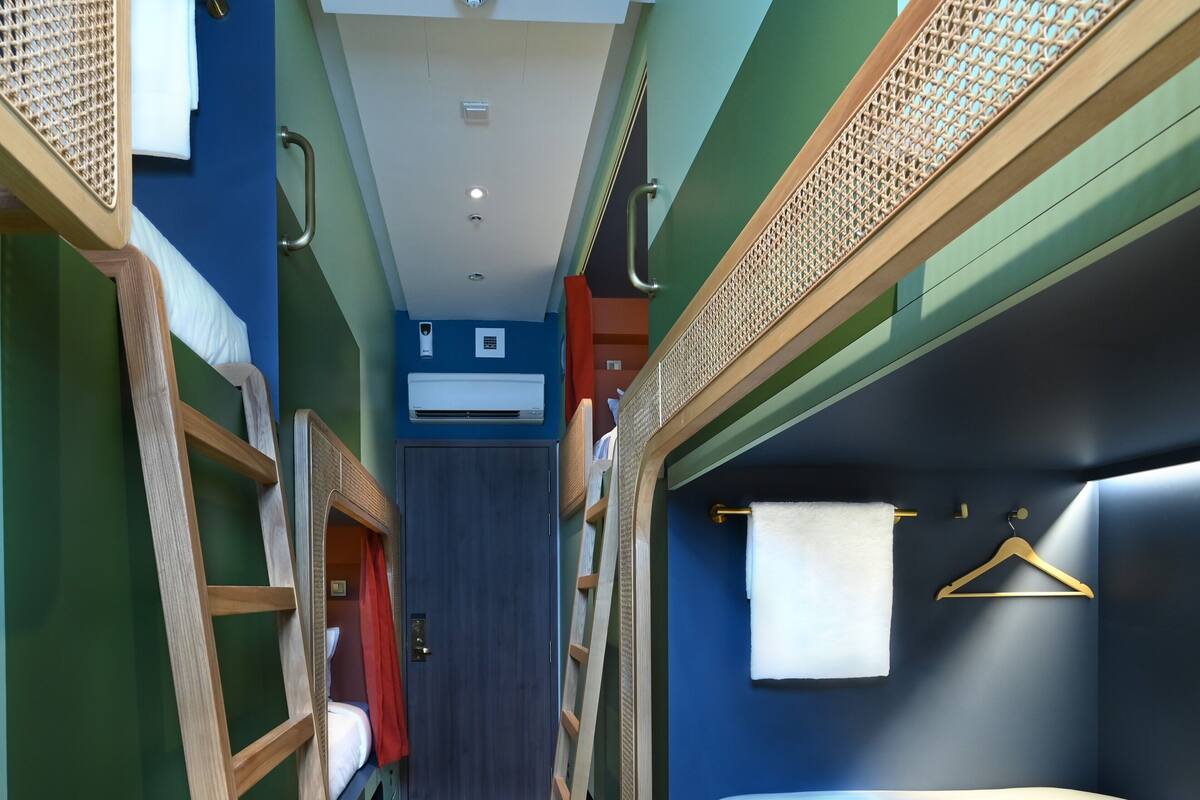 A narrow corridor with bunk beds on either side, a central door, and an air conditioning unit on the wall.