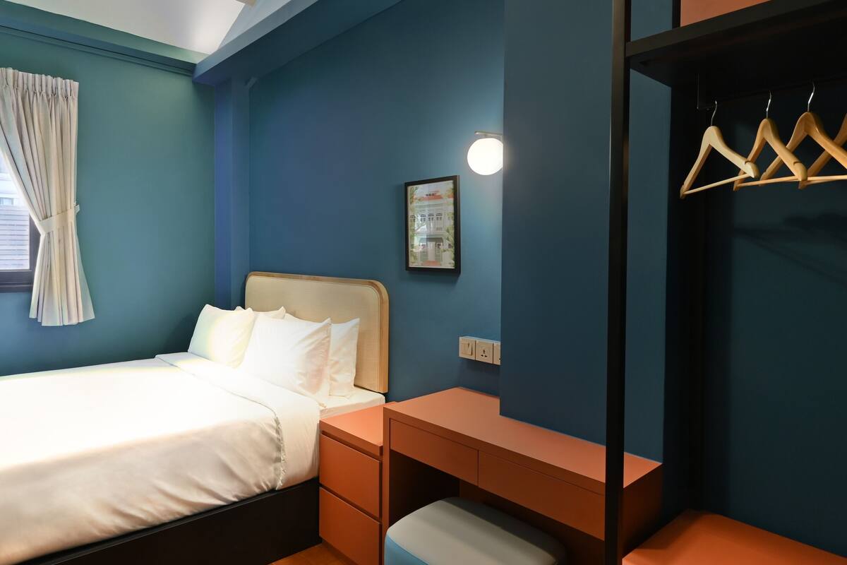 A bedroom with a bed, bedside tables, a hanging wardrobe, and a small stool.