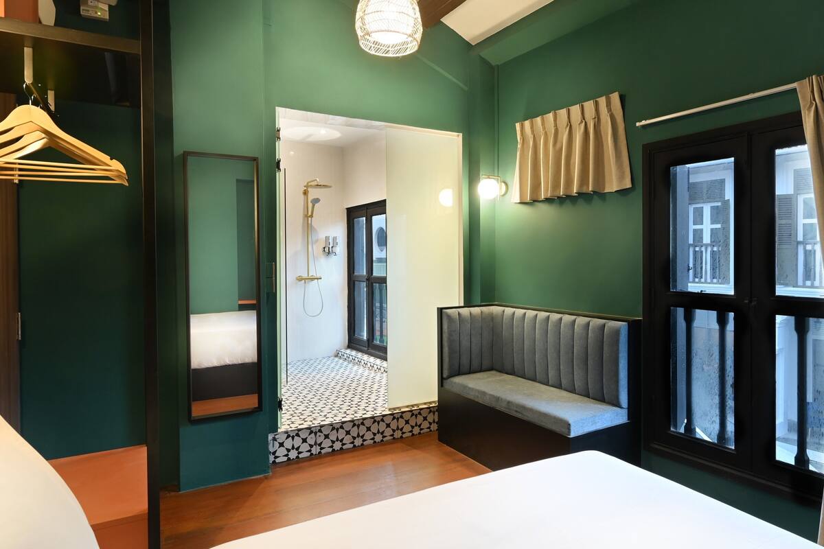 A hotel room with a bed, a seating area, a shower, and a window with curtains.