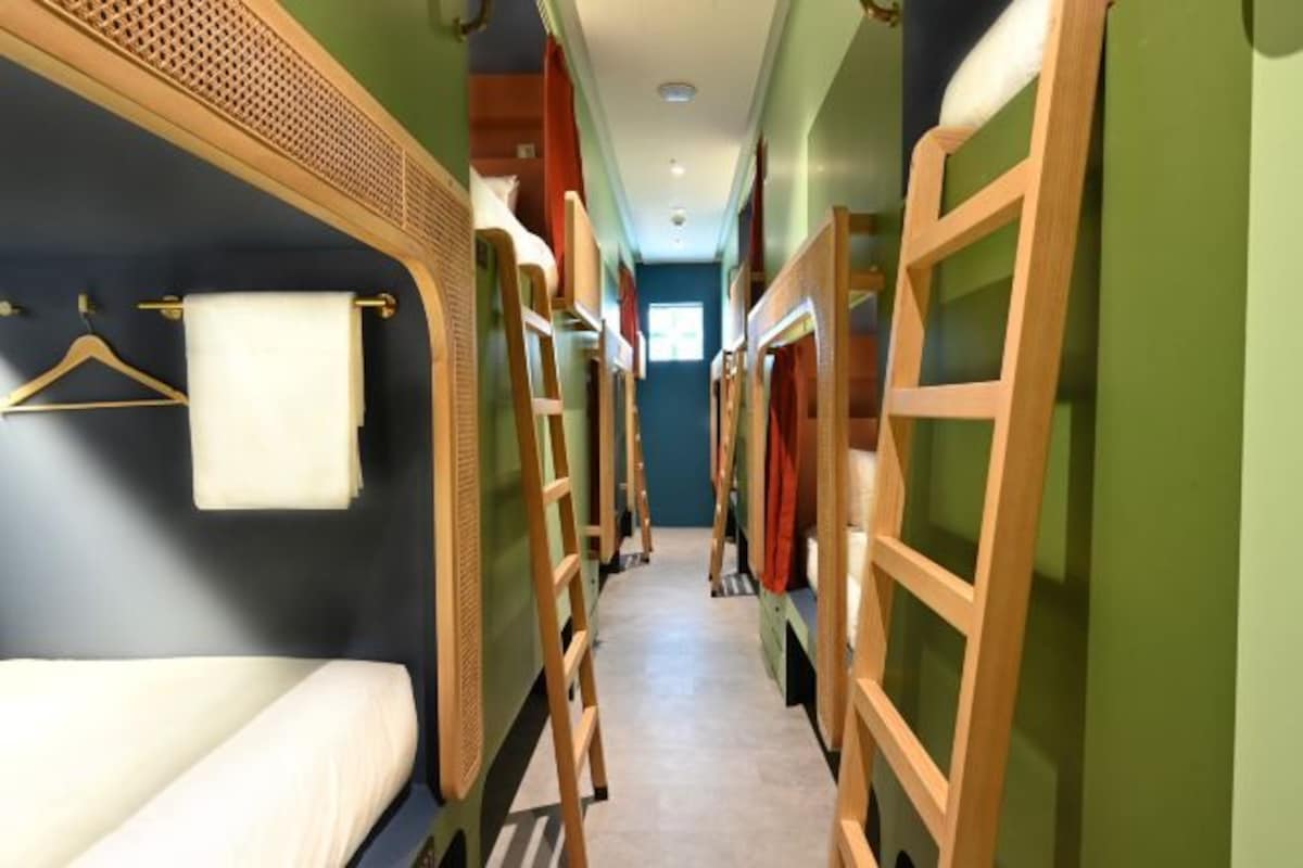 A narrow hallway with bunk beds on either side, a wooden ladder, and a towel hanging on the wall.