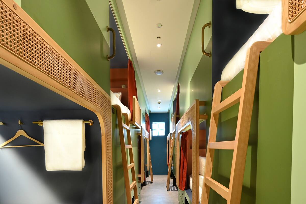 A corridor with bunk beds, wooden ladders, and a hanging towel rack.