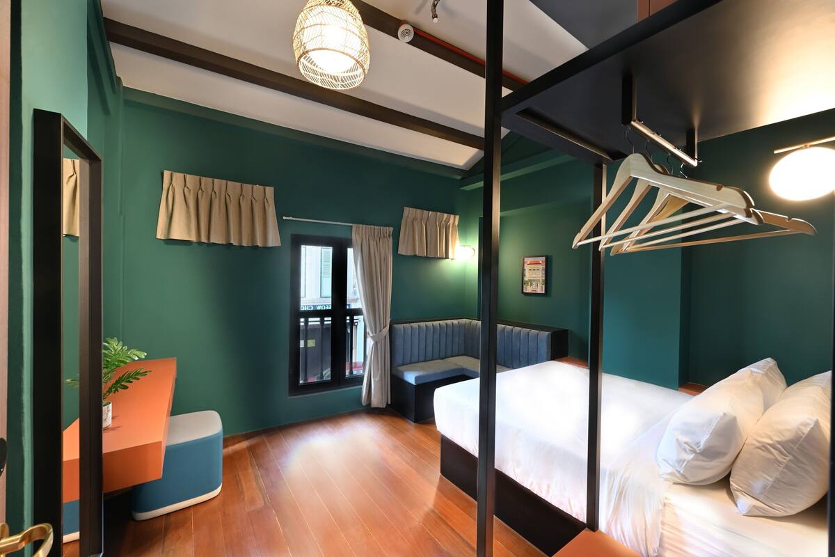 A modern bedroom with teal walls, a wooden floor, a bed with white linens, a seating area, and a hanging clothes rack.