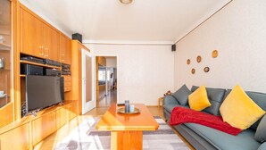 Un salon moderne avec un meuble en bois, un téléviseur à écran plat et un canapé gris agrémenté de coussins jaunes.