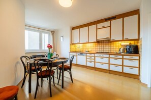 A modern kitchen with white cabinets, a dining table with chairs, and a window providing natural light.