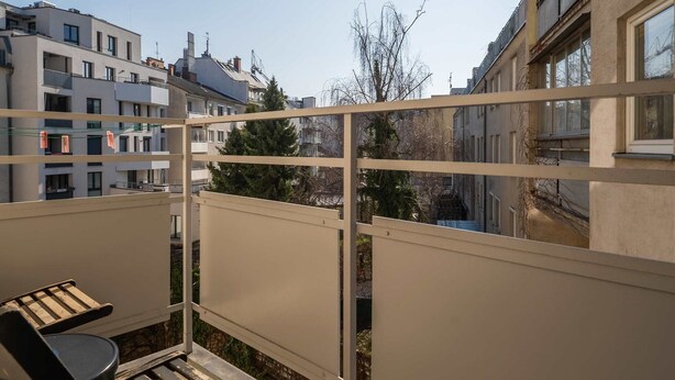 Un balcon avec une table et des chaises, une vue sur les bâtiments voisins et un ciel dégagé.