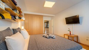 Une chambre à coucher avec un lit, des oreillers, une télévision, une bibliothèque et une armoire.