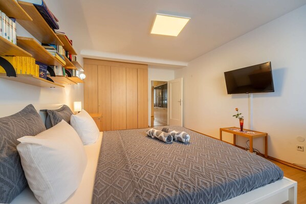 A bedroom with a bed, pillows, a TV, a bookshelf, and a wardrobe.