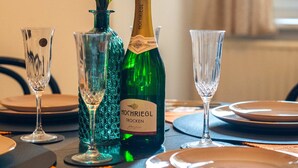 Une table à manger dressée avec des assiettes, des couverts et des verres, une bouteille de vin Hochriegl Trocken et un vase rempli de fleurs.
