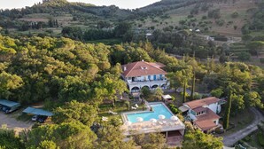 A large villa with a swimming pool, surrounded by lush greenery and hills.