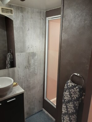 Ein Badezimmer mit einem großen Spiegel, einem Waschbecken mit Seifenschale, einem Handtuchhalter und einer Dusche mit Glastür.