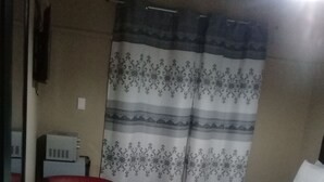 Une chambre d’hôtel avec un lit, une chaise rouge, une petite table et un rideau à motifs.