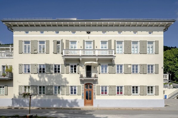 A two-story building with a balcony, a central entrance, and a row of windows with shutters.