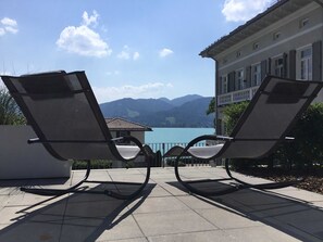 Two lounge chairs facing a lake with mountains in the background.