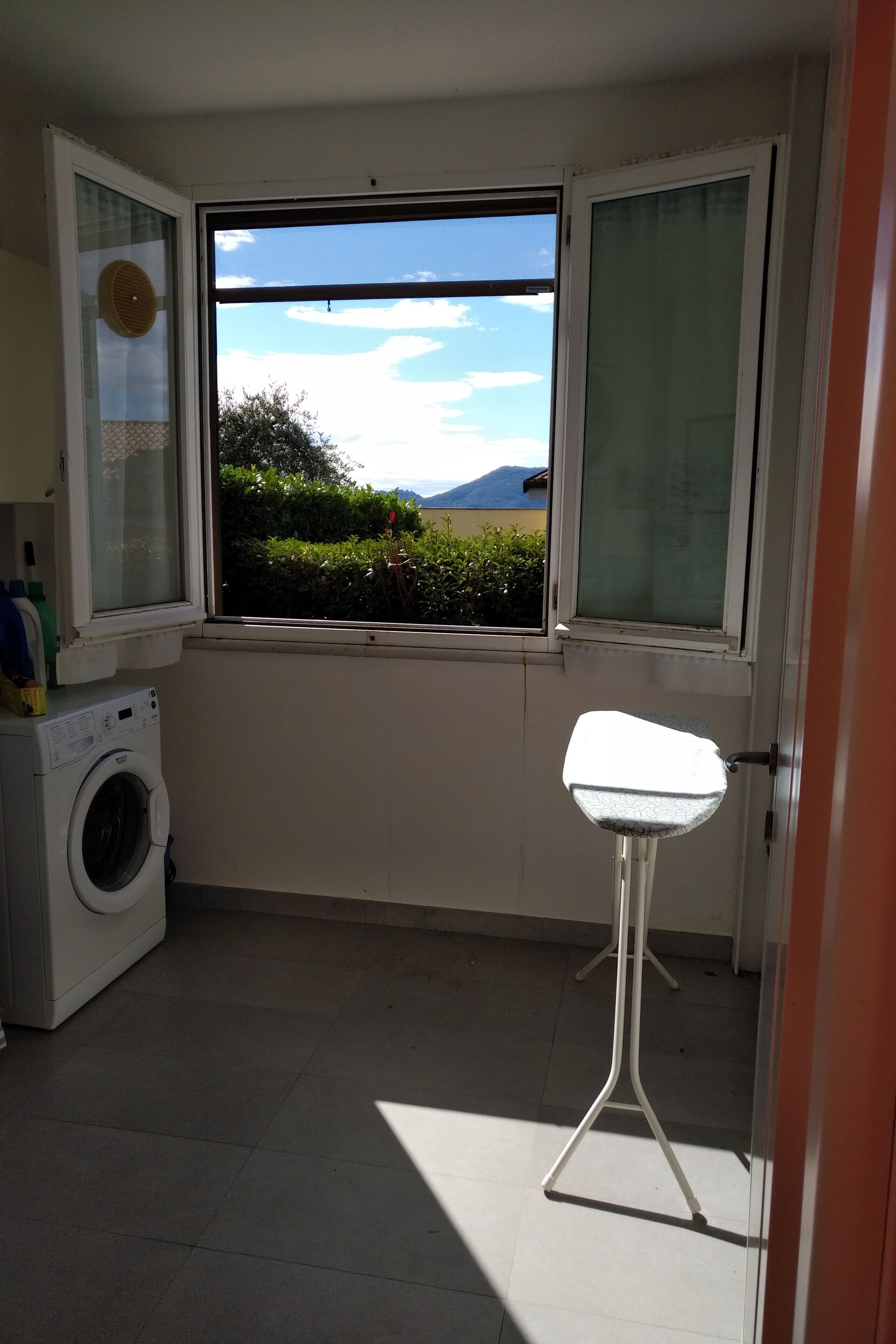 A small laundry room with a washing machine, a sink, and a window with a view of greenery and mountains.